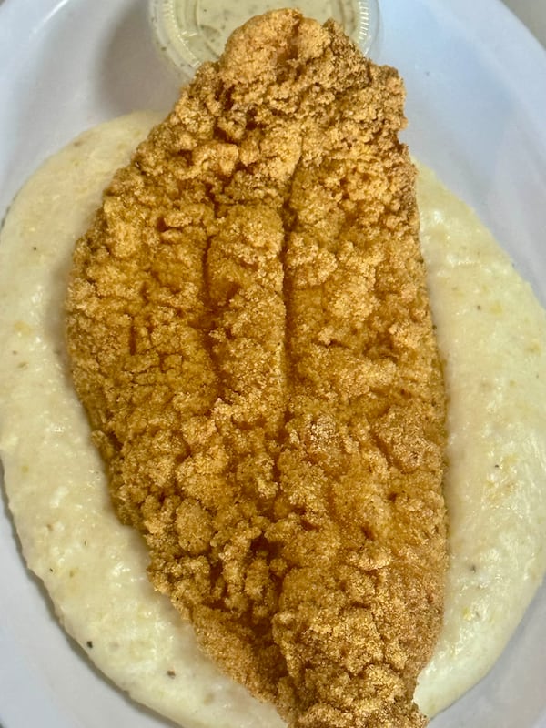 A plate of grits topped with a large filet of fried catfish.