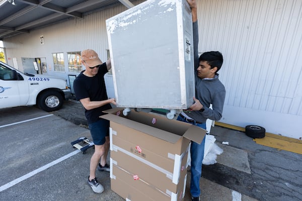 New York University student Jay Agrawal (right) packs his newly purchased galley cart from the Delta Flight Museum Surplus Sale in Atlanta on Friday, Oct. 10, 2025. He plans to check the cart on the flight to New York in his homemade box. (Arvin Temkar/AJC)
