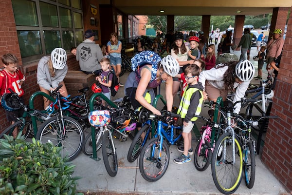 Participants in the weekly Parkside Elementary School “bike bus” help lock their kids bikes at the school. (Ben Gray for the AJC 2024)