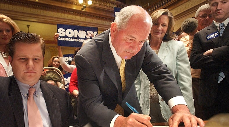 060424 ATLANTA, GA: With Georgia First Lady Mary Perdue looking over his shoulder, Gov. Sonny Perdue qualifies for governor in Senate chambers at the Georgia Capitol Monday 4/24/2006. At left is Paul Bennecke (cq), executive director of the Georgia Republican Party. (BITA HONARVAR/STAFF)