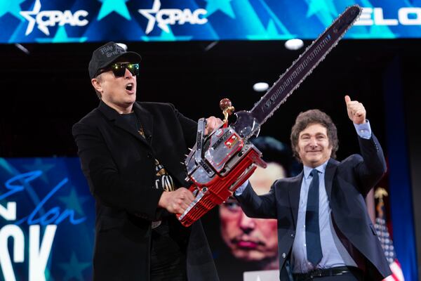 Elon Musk holds up a chainsaw at the Conservative Political Action Conference in Maryland, where he talked about the Trump administration's cost-cutting efforts. The chainsaw was a gift from Argentina President Javier Milei (right).