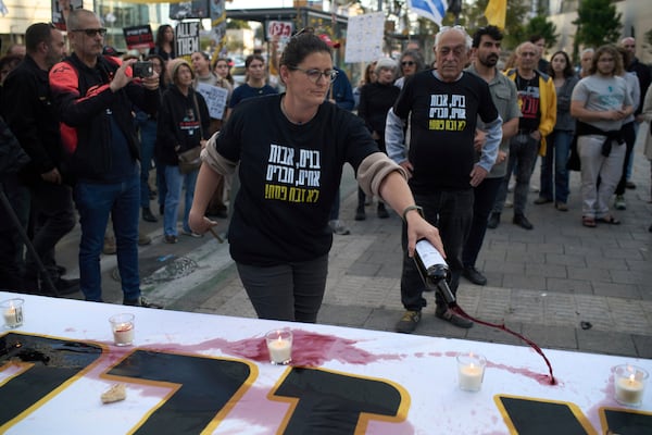 A relative of a hostage held in the Gaza Strip pours wine over a table as she takes part in a protest demanding immediate release of the hostages from Hamas captivity, during the Jewish holiday of Passover, in Tel Aviv, Israel, Saturday, April 12, 2025. (AP Photo/Leo Correa)