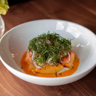A bowl holds a small salad of peaches on a bed of bright dressing topped with slivered red onions and herbs.