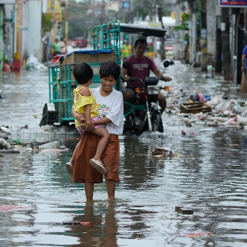A woman and child crosses a flooded street due to Typhoon Fung-wong and high tide on Monday, Nov. 10, 2025, in Navotas, Philippines. (AP Photo/Aaron Favila)