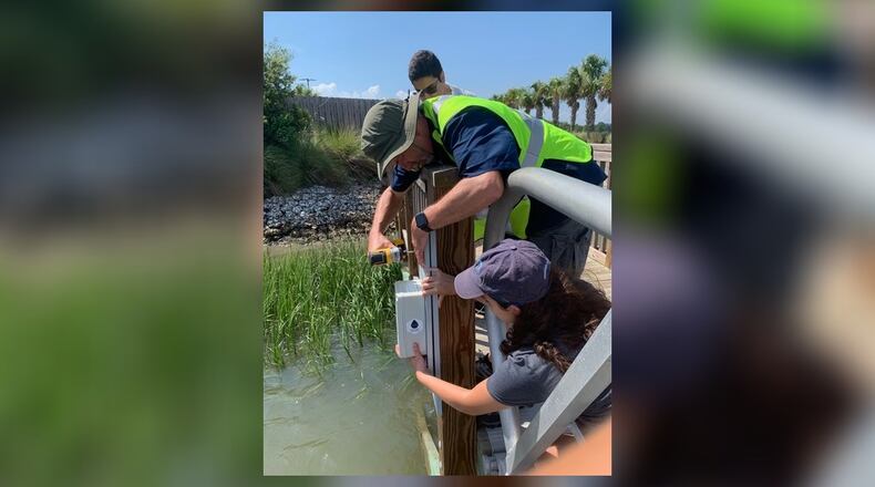 Georgia Tech students Kutub Ghandi and Maddie Carlini help Tech research scientist Russell Clark (center) install a water level sensor on July 8 at Turner Creek Boat Ramp on Whitemarsh Island. Jenkins High School engineering teacher Tom Maty partnered with Georgia Tech to build the devices, which are being placed on bridges and docks around Chatham County to record the way local flood patterns are changing as the planet warms. JADE WU/GEORGIA TECH STUDENT