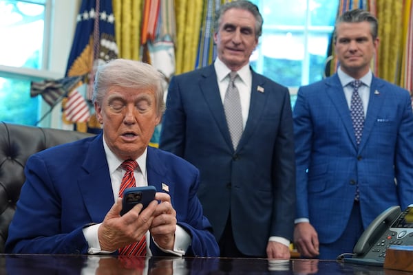President Donald Trump silences his phone that rang twice as he was speaking to reporters after signing executive orders regarding nuclear energy in the Oval Office of the White House, Friday, May 23, 2025, in Washington, as Interior Secretary Doug Burgum and Defense Secretary Pete Hegseth watch. (AP Photo/Evan Vucci)