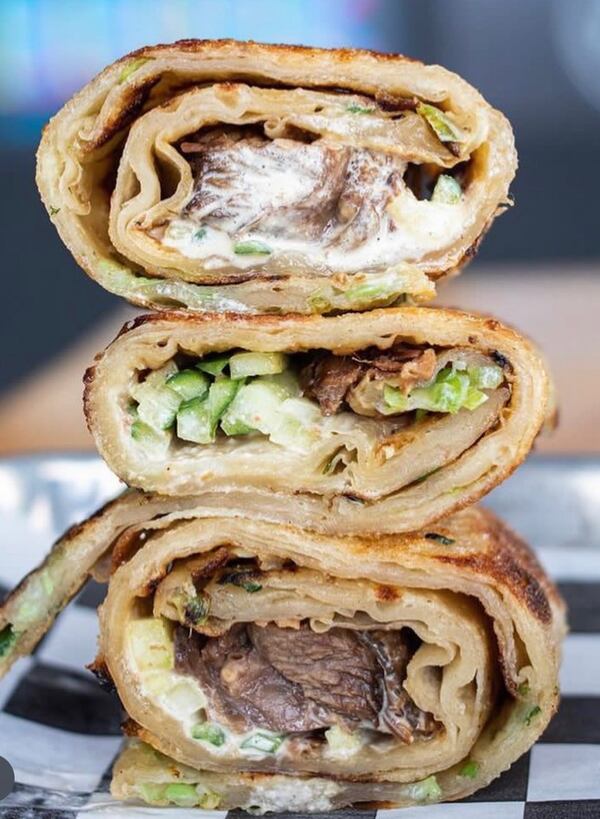 Three pancake rolls are stacked on top of each other. They are filled with what appears to be thinly sliced beef, green onions and a cream sauce.