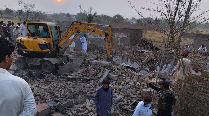 A worker clear rubble with an excavator as a police officer and local residents gather at the site of overnight suicide bombing at a security post in Fatah Khel, in Bannu, a district in Pakistan's Khyber Pakhtunkhwa province bordering Afghanistan, Sunday, May 10, 2026. (AP Photo/Aamad Khattak)
