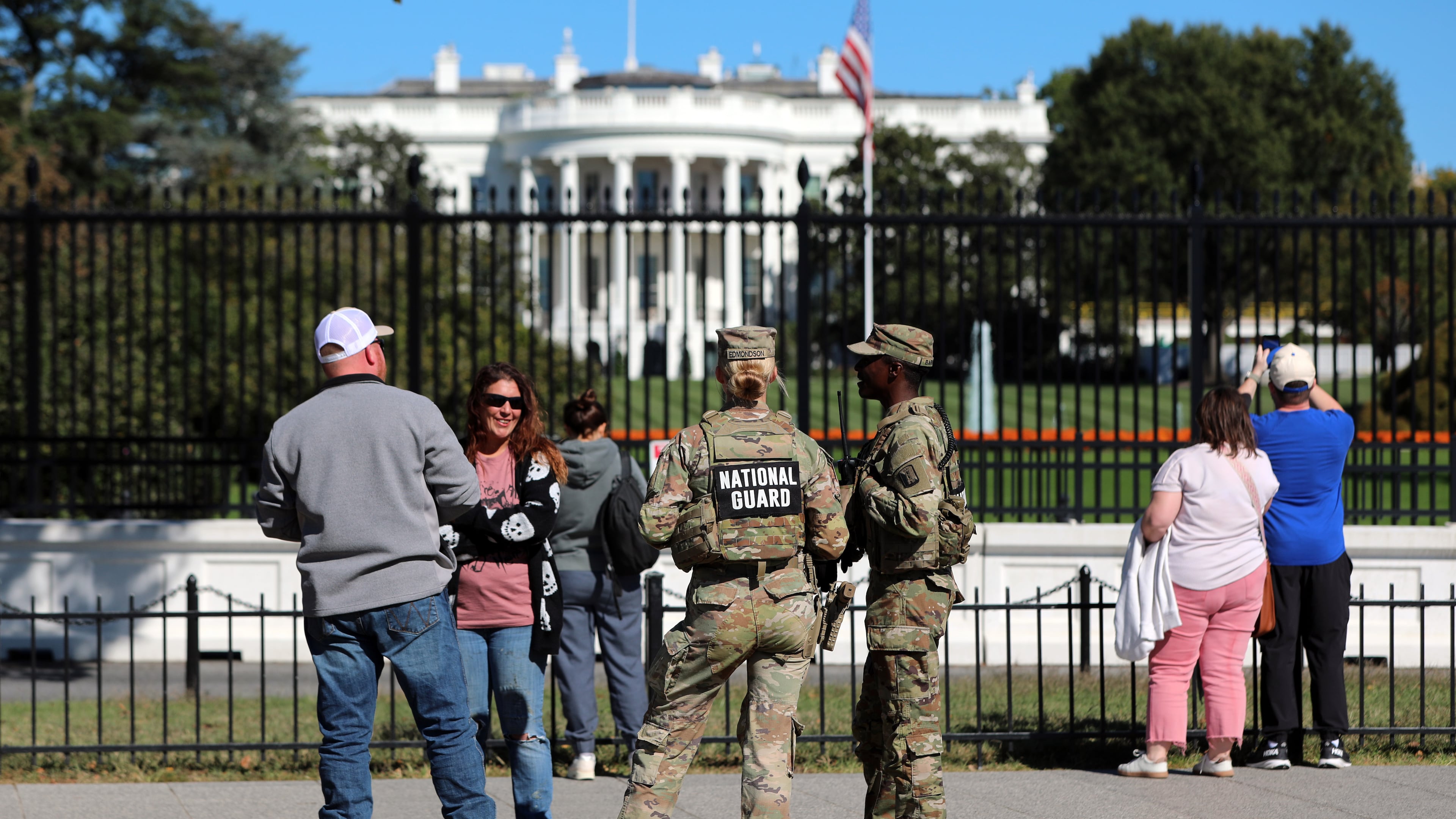 FILE - People talk with National Guard soldiers on the Ellipse, with the White House in the background, Oct. 17, 2025, in Washington. (AP Photo/Rahmat Gul, File)