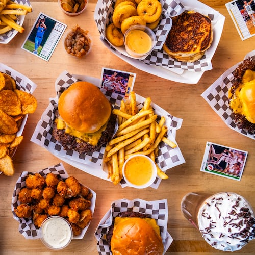 An overhead shot of a table full of food from a burger restaurant, including burgers, fries, frozen sodas, tater tots, chips and dip and sides and other accouterments.