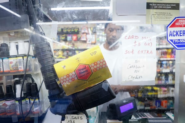 A visible semiautomatic rifle is propped behind bulletproof glass as JJ Food Mart store clerk Connell Daniels Jr. works on the westside of Atlanta. (Miguel Martinez/AJC)
