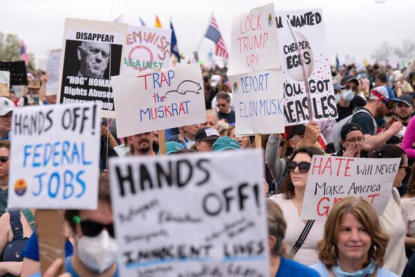 Demonstrators hold up signs during a "Hands Off!" protest against President Donald Trump at the Washington Monument in Washington, Saturday, April 5, 2025. (AP Photo/Jose Luis Magana)