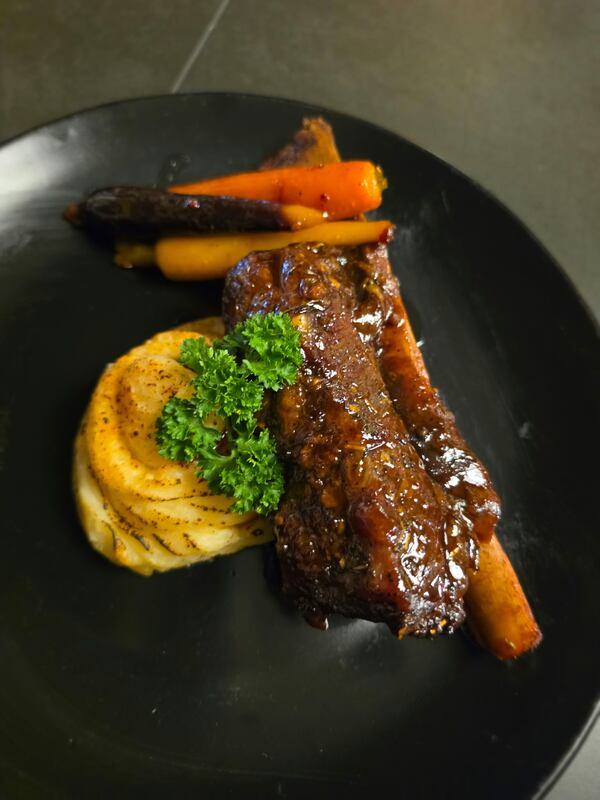 Beef short rib with carrots and mashed potatoes on a black plate