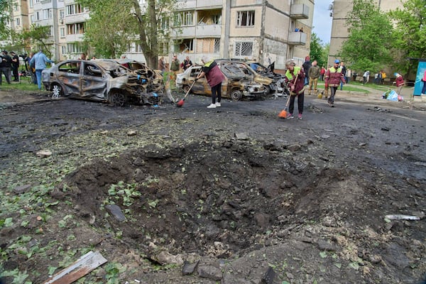 Municipal workers clean up near burnt cars and a crater made by a drone in the residential area following Russia's air raid in Kyiv, Ukraine, Sunday, May 4, 2025. (AP Photo/Efrem Lukatsky)