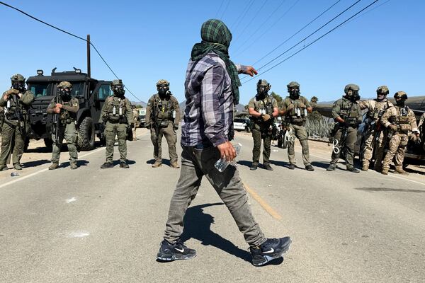 A demonstrator walks in front of federal agents blocking a road during an immigration raid in Camarillo, Calif. (AP Photo/Michael Owen Baker)