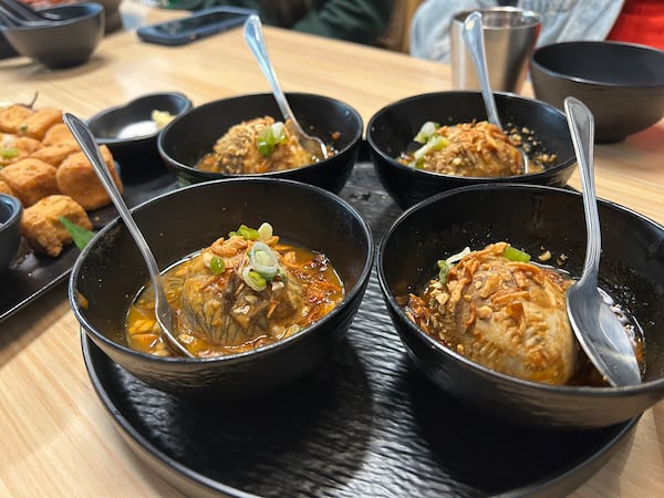 Four black bowls filled with balut, tamarind sauce and topped with fried shallots.