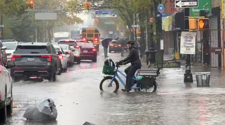 A cyclist rides through floodwaters during a rainstorm in New York, Thursday, Oct. 30, 2025. (AP Photo/David Martin)