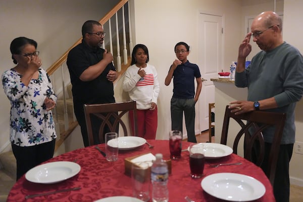 The Rev. Ricky Malebranche, second from left, makes the sign of the cross as he leads prayers before a family meal at his home in Gainesville, Va., on Sunday, May 25, 2025. (AP Photo/Luis Andres Henao)