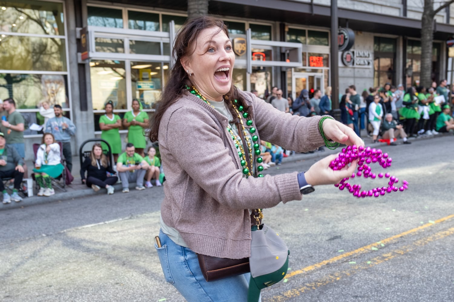 Erica Dixon, who wasn’t an official entrant in the Atlanta St. Patrick’s Parade, throws beads to spectators along Peachtree Street on Saturday, March 14, 2026. (Ben Gray for the AJC)