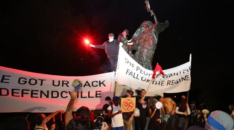 After marching from Woodruff Park to Piedmont Park during a anti white nationalism memorial and march in response to violence in Virginia, protesters climb and spray paint a Confederate monument on Sunday, Aug. 13, 2017, in Atlanta. The peace monument at the 14th Street entrance depicts a angel of peace stilling the hand of a Confederate soldier about to fire his rifle. (Curtis Compton/Atlanta Journal-Constitution/TNS)