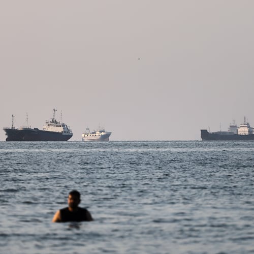 A person stands in shallow water as cargo and commercial vessels are anchored in the Strait of Hormuz off Bandar Abbas, Iran, Monday, June 8, 2026. (Amirhosein Khorgooi/ISNA via AP)