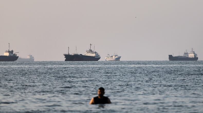 A person stands in shallow water as cargo and commercial vessels are anchored in the Strait of Hormuz off Bandar Abbas, Iran, Monday, June 8, 2026. (Amirhosein Khorgooi/ISNA via AP)