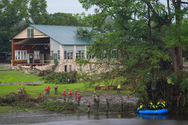 Rescue workers are seen on land and on a boat as they search for missing people near Camp Mystic along the Guadalupe River after a flash flood swept through the area Sunday, July 6, 2025, in Hunt, Texas. (AP Photo/Julio Cortez)