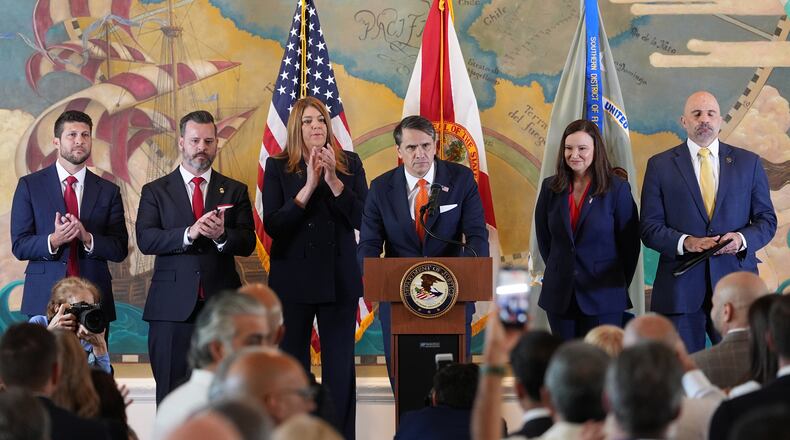 Audience members give a standing ovation as Acting Attorney General Todd Blanche, center, speaks at an event where federal prosecutors announced charges against former Cuban President Raul Castro in the 1996 downing of civilian planes operated by Miami-based exiles, Wednesday, May 20, 2026, in Miami. Also shown, from left, are, Florida Attorney General James Uthmeier; Jason A. Reding Quiñones, U.S. attorney for the southern district of Florida; Miami Dade College President Madeline Pumariega; Sen. Ashley Moody, R-Fla.; and FBI Deputy Director Christopher Raia. (AP Photo/Rebecca Blackwell)