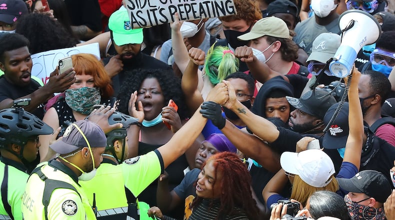 Showing respect and solidarity, an Atlanta Police officer in a bicycle unit joins hands with a protester during a street face off outside the CNN Center at Olympic Park during a fifth day of protests over the death of George Floyd on Tuesday. Some major companies in Atlanta have recently spoken out against racial injustice. Curtis Compton ccompton@ajc.com