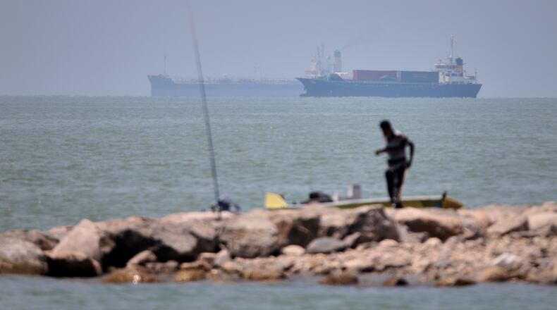 A man stands beside a fishing pole along the shore as cargo ships and commercial vessels are seen in the Strait of Hormuz off Bandar Abbas, Iran, Wednesday, June 17, 2026. (Amirhosein Khorgooi/ISNA via AP)