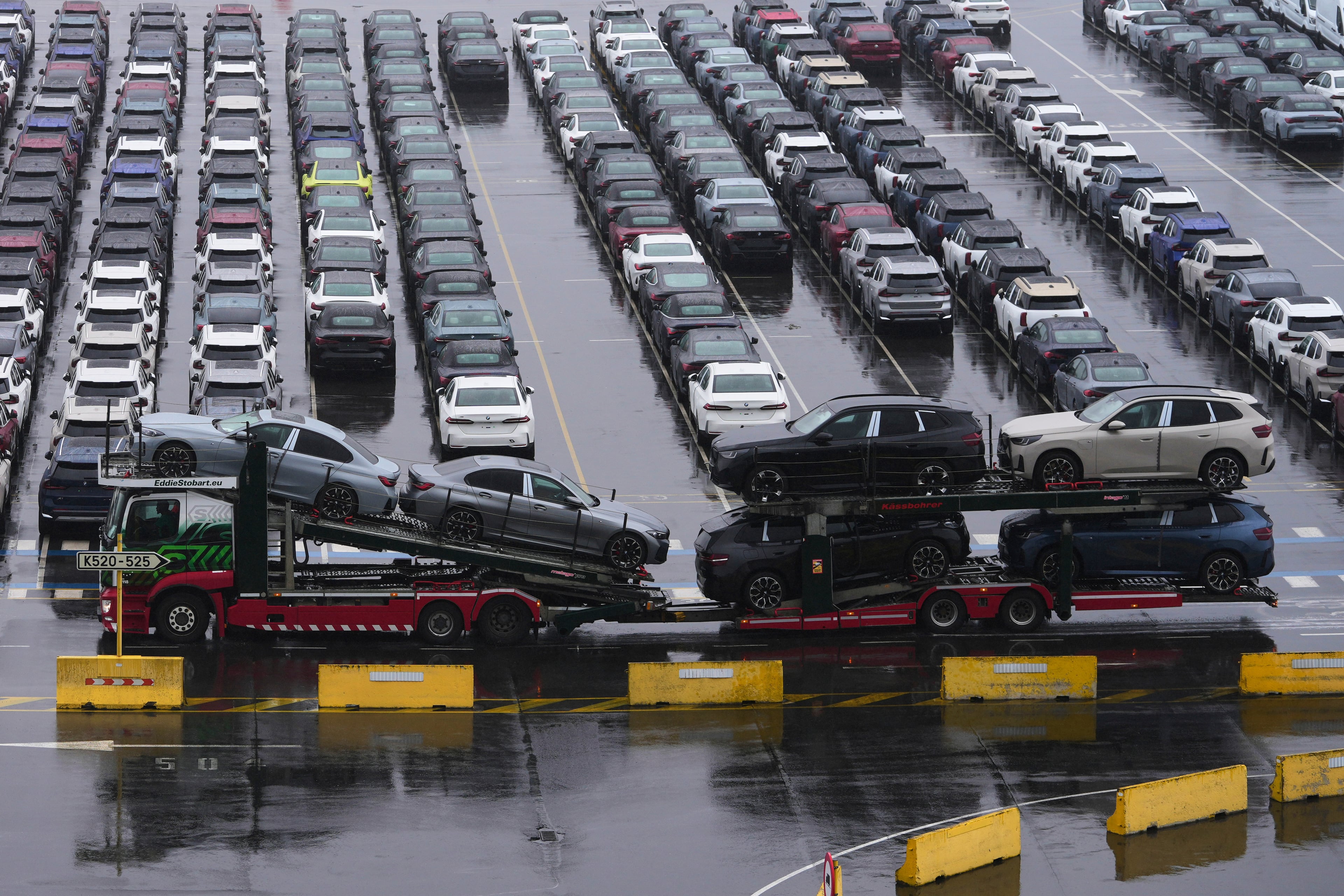 A car carrier drives past new cars parked in a lot at the International Car Operators terminal in the Port of Zeebrugge, Belgium, Thursday, July 31, 2025. (Virginia Mayo/AP)