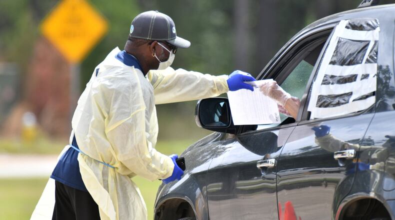 A medical worker in protective gear helps a potential COVID-19 patient with paperwork at a Phoebe Putney Health System drive-through testing site in Albany on Tuesday, March 24, 2020. HYOSUB SHIN / HYOSUB.SHIN@AJC.COM