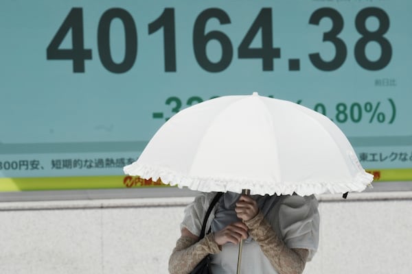 A person walks under the intense sun near an electronic stock board displaying Japan's Nikkei index at a securities firm Tuesday, July 1, 2025, in Tokyo. (AP Photo/Eugene Hoshiko)