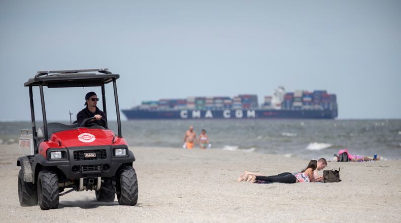 A member of the Tybee Island Life Guards patrols the beach on a ATV while visitors sunbathe in the sand on Saturday, April 4, 2020. (Photo: Stephen B. Morton/Special to the AJC)