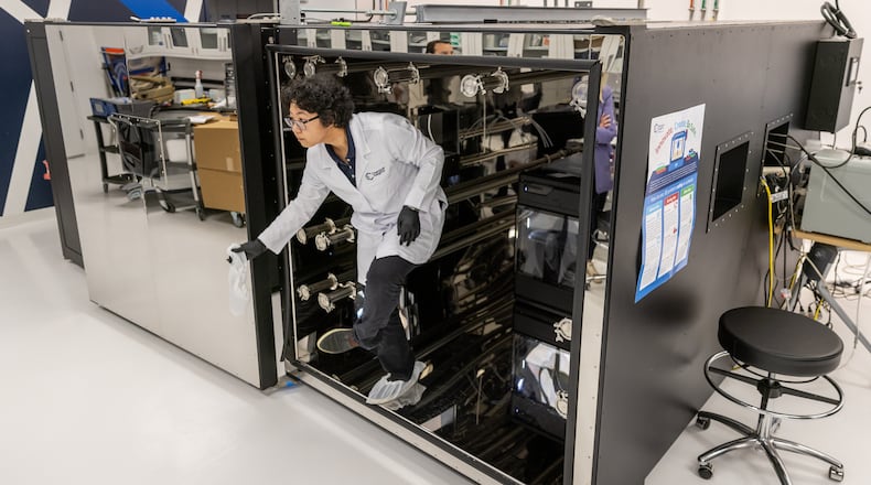 Dr. Qian Zhang, with Chemical Insights Research Institute, emerges from a 5-foot, 10-inch-tall, by 9-foot, 7-inch-long airtight chamber before sealing it. She and other scientists at the Marietta research facility were using the enclosure to test the ability of a newer-model 3D printer inside to capture pollutants with its built-in filtration unit, on March 26, 2024. She and other researchers have documented potentially harmful emissions from 3D printers without such filters, which are more common. (Steve Schaefer/steve.schaefer@ajc.com)