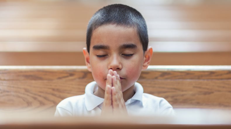 Schoolboy praying with eyes closed in empty church