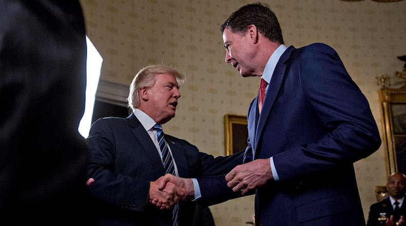 U.S. President Donald Trump (C) shakes hands with James Comey, director of the Federal Bureau of Investigation (FBI), during an Inaugural Law Enforcement Officers and First Responders Reception in the Blue Room of the White House on January 22, 2017 in Washington, DC. Trump today mocked protesters who gathered for large demonstrations across the U.S. and the world on Saturday to signal discontent with his leadership, but later offered a more conciliatory tone, saying he recognized such marches as a "hallmark of our democracy." (Photo by Andrew Harrer-Pool/Getty Images)