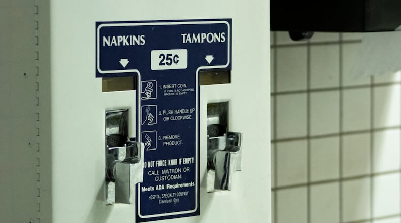 feminine hygiene product dispenser in bathroom with blue labels saying pad and tampon for 25 cents