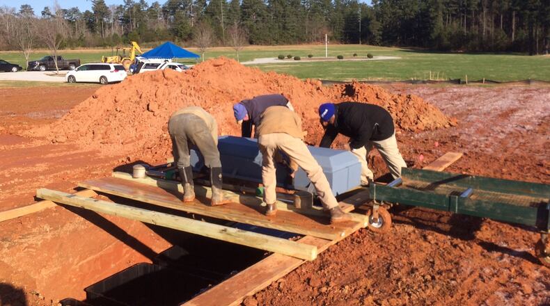 Rev. Cliff Dawkins, right with blue hat, and a crew at Lakeside Memorial Gardens Cemetery position a casket for burial. Photo by Bill Torpy
