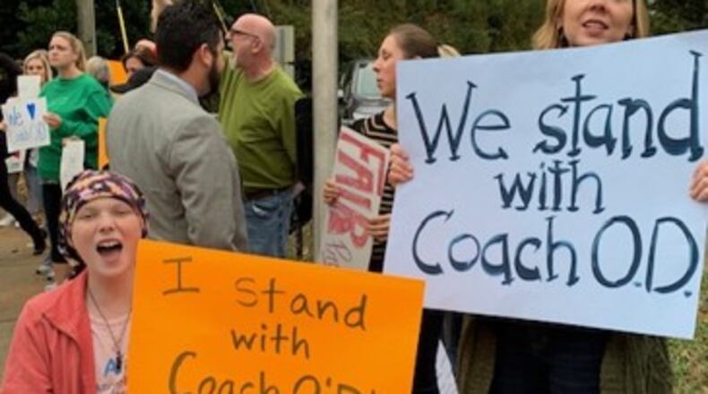 Supporters of a suspended Henderson Mill Elementary School coach want him fully vindicated and reinstated now, but DeKalb has not done so.