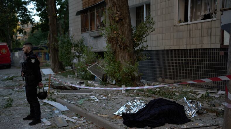 A policeman stands next to the bodies of two people killed during an overnight Russian attack in Kyiv, Ukraine, Thursday, Aug. 20, 2026. (AP Photo/Francisco Seco)