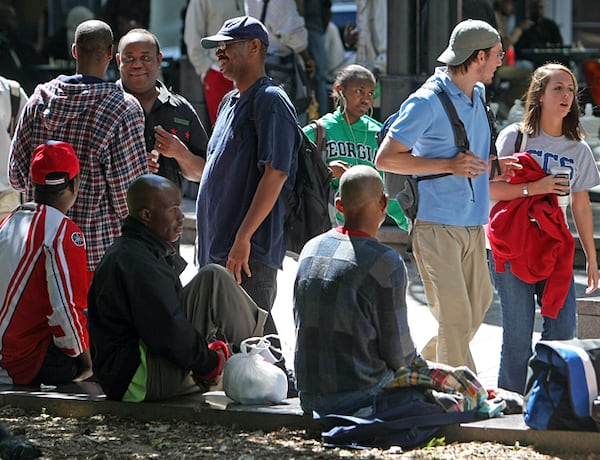 In this file photo, pedestrians walk by several homeless people hanging out at Woodruff Park during a mid-week afternoon in Atlanta.