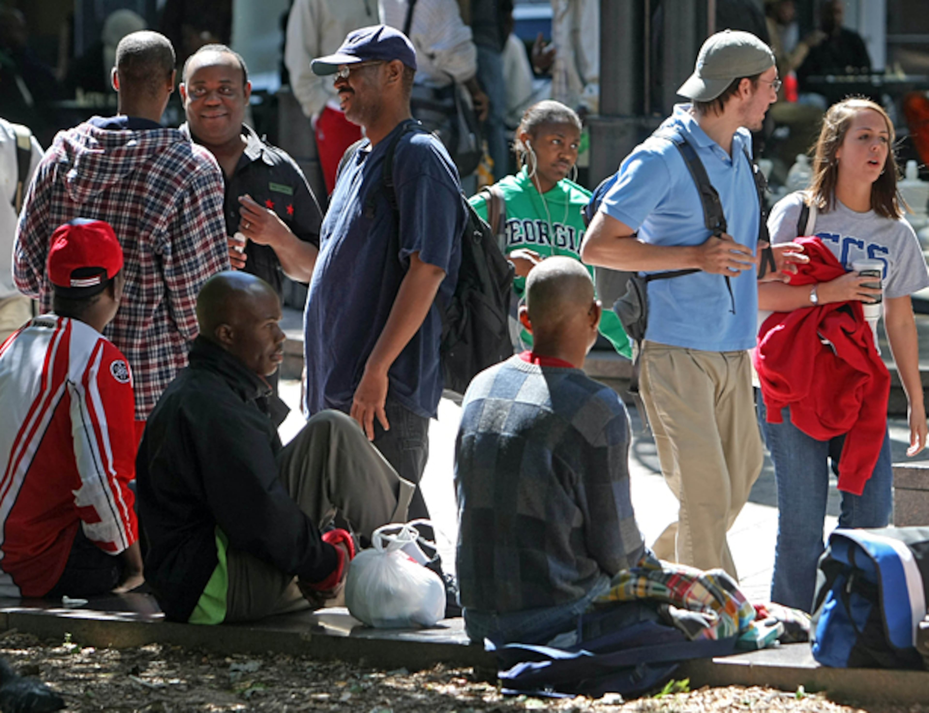 In this file photo, pedestrians walk by several homeless people hanging out at Woodruff Park during a mid-week afternoon in Atlanta.
