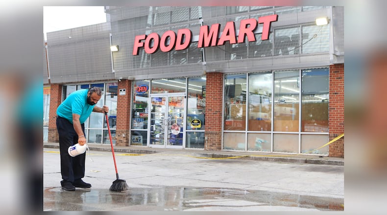 Food Mart owner Kuldip Rakkar pours bleach on a pool of blood following a shooting outside the Old National Highway business Tuesday.