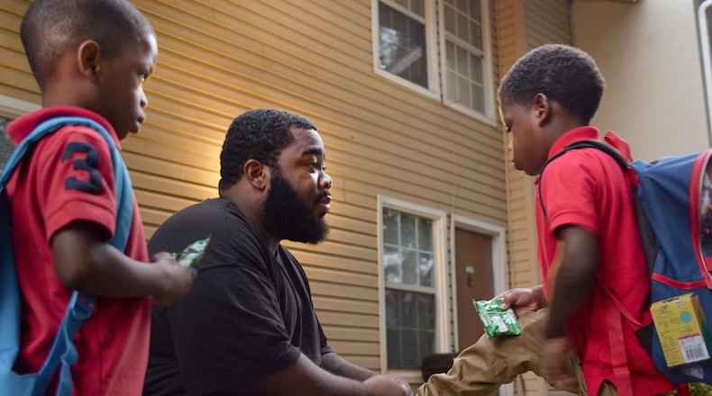 Marquez Kemp holds his foot up so his father Markevius Kemp, can tie his shoe as younger brother Micah looks on. Natrice Miller/Freelance (AJC archive photo)