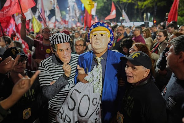 Supporters of Brazilian President Luiz Inacio Lula da Silva, wearing masks of U.S. President Donald Trump and former President Jair Bolsonaro as a prisoner, protest Trump's announcement of 50% tariffs on Brazil, in São Paulo, Thursday, July 10, 2025. (AP Photo/Andre Penner)