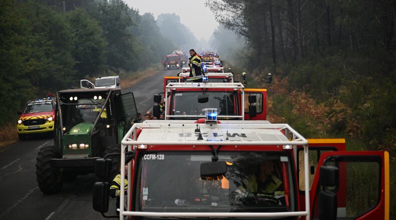 A firefighter stands on a truck on a road near Lacanau, southwestern France, Saturday, July 25, 2026, as wildfires rage in the area. (AP Photo/Emma Da Silva)