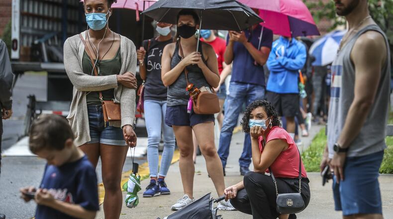 Stephanie Herrera crouches in line as she and other voters lined up in the rain on Friday, June 6, 2020 at Garden Hills Elementary School located at 285 Sheridan Drive NE, in Atlanta. Some waited up to three hours to vote. JOHN SPINK/JSPINK@AJC.COM