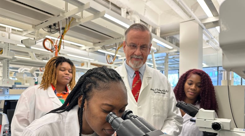 Dr. Barney Graham watches with Morehouse School of Medicine students Briana Brock, left and Dana Battle, right, as Morehouse School of Medicine student Aww Sore looks into a microscope .