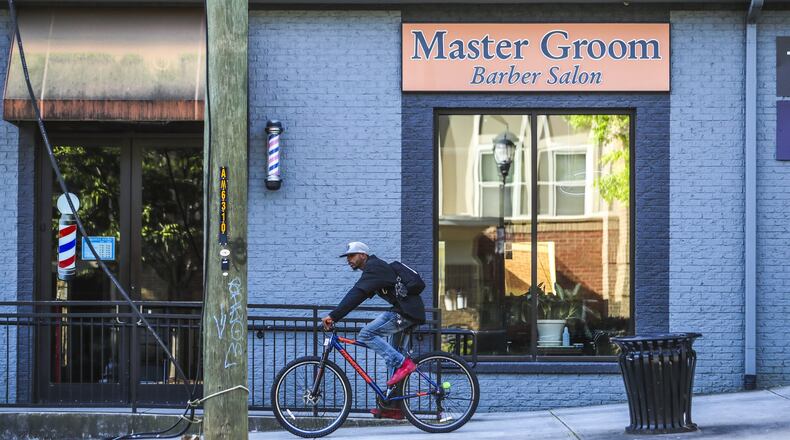 A bicycle rider pedals past the Master Groom Barber Salon in the 300 block of Decatur Street on Wednesday, April 22, 2020. Gov. Brian Kemp has defended rolling back restrictions on small businesses such as barber shops and hair salons despite federal health officials and many mayors of Georgia cities warning that it is too soon to relax measures meant to quell the coronavirus pandemic. JOHN SPINK/JSPINK@AJC.COM